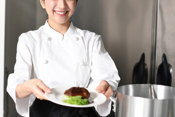 肉料理を提供する若いアジア人の女性調理師