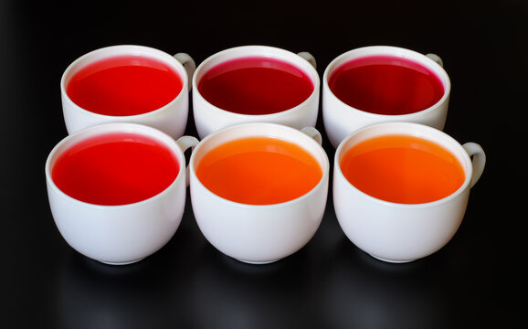 Six white cups with sweet dessert jelly (cherry, strawberry and orange), installed on a black surface, close-up