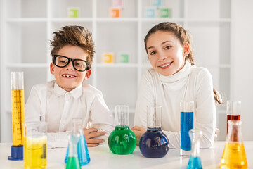 Two smiling children in a chemistry class engaging with colorful beakers and flasks, showcasing a fun and educational environment.