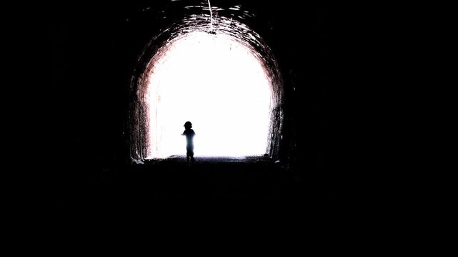 Kid running along a creepy dark tunnel to a bright light. Metaphor of life and death