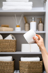 Hand holding toilet paper roll against bathroom cabinet on background