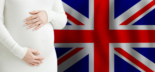  Pregnant woman belly against Flag of the United Kingdom background. Demographics and pregnancy in...