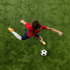 Top view photo of young sporty woman, football athlete preparing to kick ball in motion on green...
