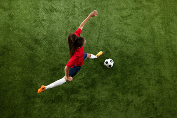 Top view photo of young sporty woman, football athlete preparing to kick ball in motion on green...
