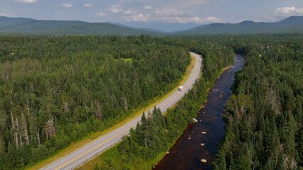 Traveling and Driving on highway by clear water creek in New Hampshire mountains  with green trees and natural countryside
