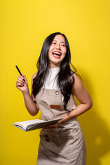 A woman is smiling and holding a pen and a book