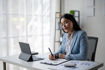 A woman is sitting at a desk with a laptop and a pen