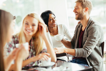 Diverse young friends drinking coffee in busy cafe