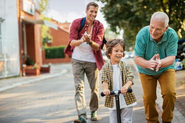 Father and grandfather teaching boy to ride a scooter outdoors
