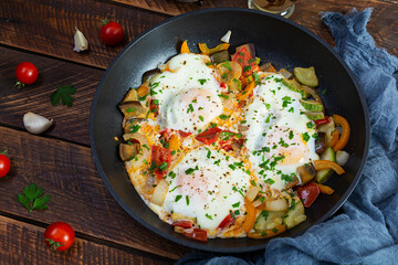 Shakshuka in a frying pan.  Fried eggs with tomato, pepper, zucchini and herbs
