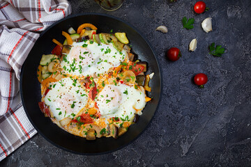 Shakshuka in a frying pan.  Fried eggs with tomato, pepper, zucchini and herbs