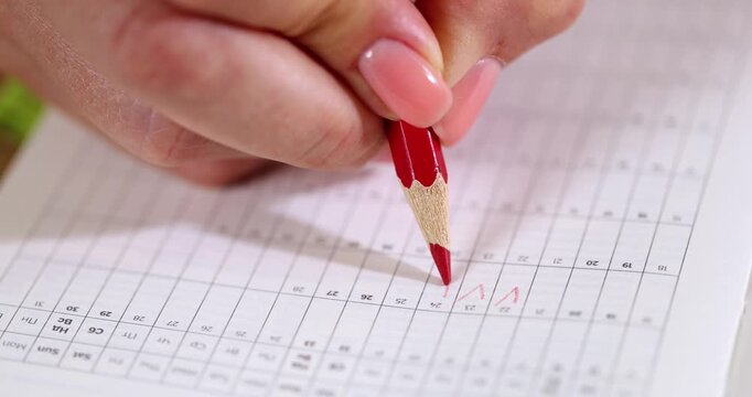Female hand marks days of menstrual cycle in calendar with red pencil closeup 4k movie slow motion. Pregnancy planning ovulation tracking concept