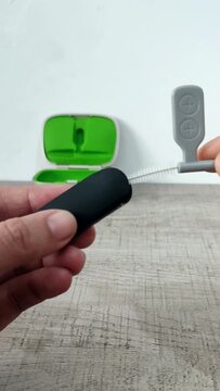 A woman's hand holds a brush to clean the wireless microphone receiver used as an assistive hearing device for users of hearing aids or cochlear implants