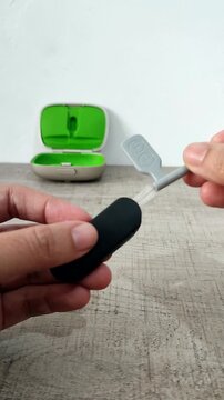 A woman's hand holds a brush to clean the wireless microphone receiver used as an assistive hearing device for users of hearing aids or cochlear implants