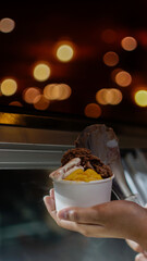 Close up hand of a person scooping ice cream in to a paper bowl with blurred background