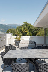 External balcony of villa modena with a small living room composed of a sofa, two armchairs and a table with chairs. In the background Swiss hills