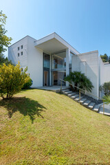 Green garden and entrance of a white modern house. Sunny summer day and blue sky