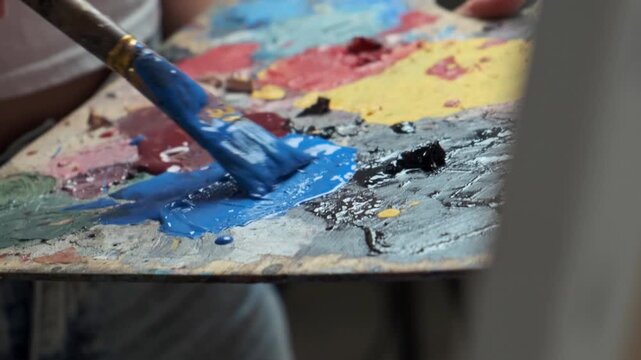 Close-up palette of an artist painting with acrylic or oil paints. Artist mixes paints