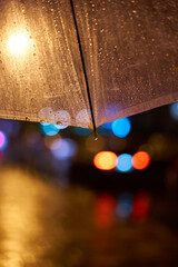 Rainy evening under an umbrella illuminating city lights and reflections on the street