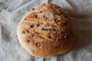 Homemade sourdough bread with raisins, with cracked, slits and baked with a crust on fabric, top...