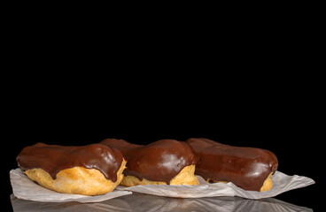 Three eclairs with cream, macro, isolated on a black background.