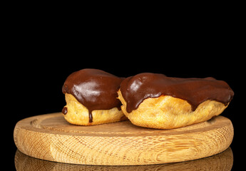 Two eclairs with cream on a wooden tray, macro, isolated on black background.