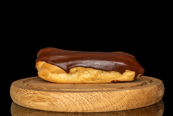One eclair with cream on a wooden tray, macro, isolated on black background.