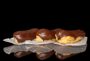 Three eclairs with cream, macro, isolated on a black background.