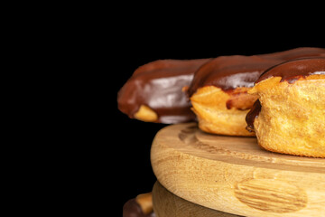 Three eclairs with cream on a wooden tray, macro, isolated on black background.