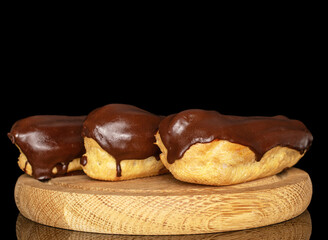 Three eclairs with cream on a wooden tray, macro, isolated on black background.