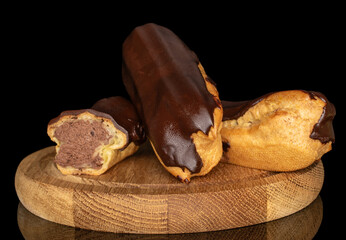 Three eclairs with cream on a wooden tray, macro, isolated on black background.