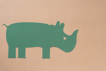 machine-cut green paper rhinoceros on a light pastel brown background with space for copy