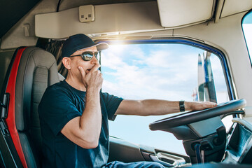Handsome experienced male truck driver with a hat sitting and driving his truck. Professional...