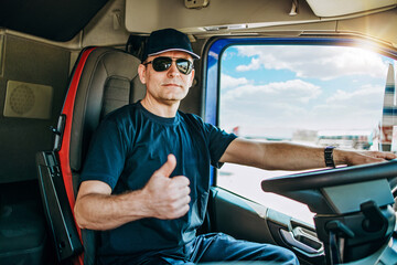 Handsome experienced male truck driver with a hat sitting and driving his truck. He is looking at...