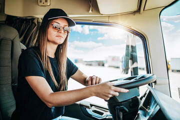 Portrait of beautiful young woman professional truck driver sitting in a big truck and looking at...