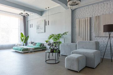 stylish discreet interior of the sleeping area in a modern studio in white-gray colors with green plants. daylight and no people inside