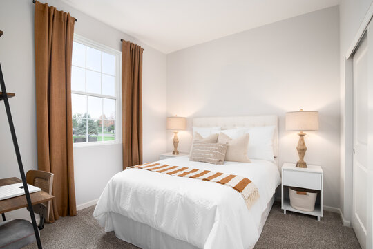 A cozy bedroom with brown, orange, and white bedding, two lamps on white nightstands, and a small desk and chair.