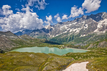 view from above of the green lake goillet in summer sunshine with the alps in the background under a blue sky with a few nice clouds
