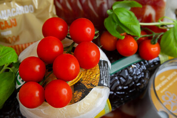 Food set in a straw basket: cherry tomatoes, small head of cheese, jamon, basil, liqueur, figs, scented candle; gift idea 