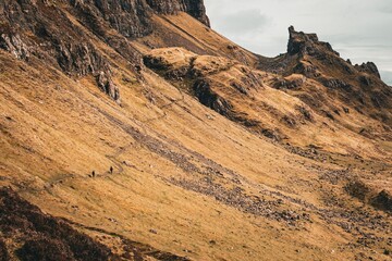 Fototapeta premium Hikers walking on a trail in a mountainous landscape with rugged terrain and a cloudy sky.