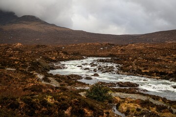 Scenic view of a rugged landscape with a flowing river under a cloudy sky in the Scottish Highlands