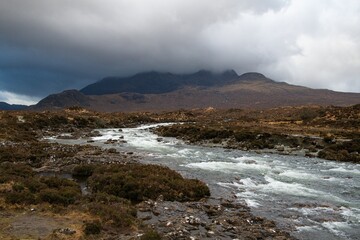Scenic view of a river flowing through a rocky landscape with a mountain shrouded in clouds