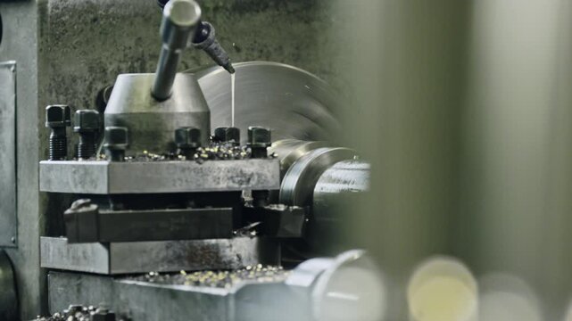 Metalworking lathe machine precisely cutting a cylindrical object in an industrial workshop. Close-up view showing cutting tool engaging with metal workpiece