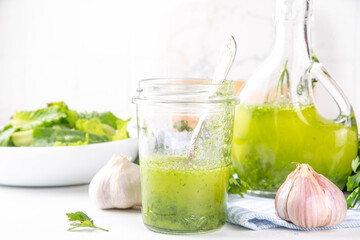 Culinary aromatic Green Herb Salad Dressing. Infused fresh Basil, parsley garlic olive oil for cooking dinner, with green salad on kitchen background copy space