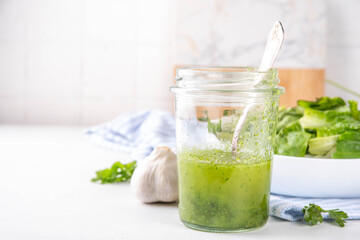 Culinary aromatic Green Herb Salad Dressing. Infused fresh Basil, parsley garlic olive oil for cooking dinner, with green salad on kitchen background copy space