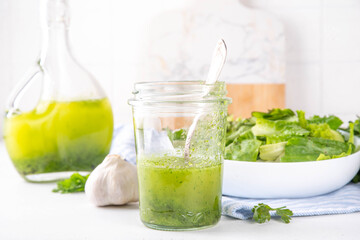 Culinary aromatic Green Herb Salad Dressing. Infused fresh Basil, parsley garlic olive oil for cooking dinner, with green salad on kitchen background copy space