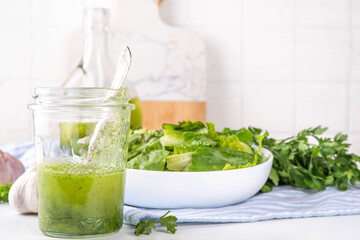 Culinary aromatic Green Herb Salad Dressing. Infused fresh Basil, parsley garlic olive oil for cooking dinner, with green salad on kitchen background copy space