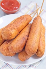 Stack of corn dogs on white plate, served with ketchup, vertical closeup