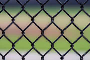 Fototapeta premium Tight photo of a chain link fence taken at a baseball field during bright daylight with green grass in the background.