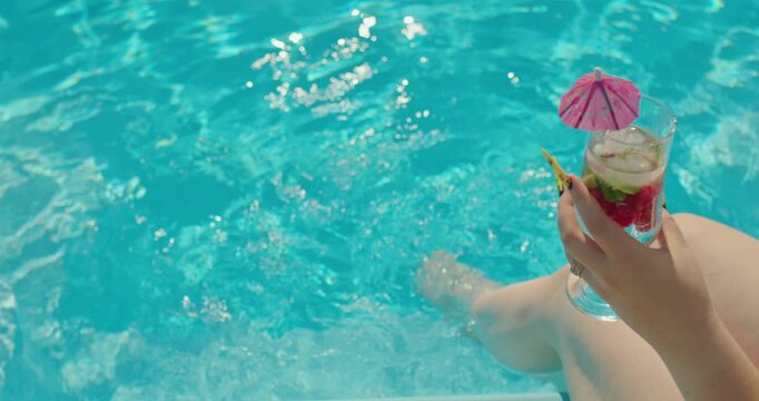 Woman's hand holds a cocktail in the background of the pool